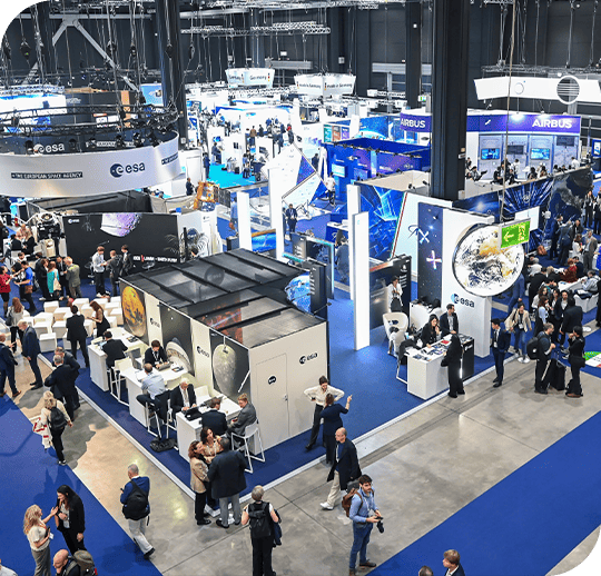 erial view of a busy expo hall with multiple booths, attendees networking and exploring technology displays at a trade or industry exhibition.