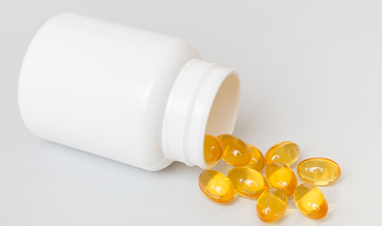 Yellow soft gel capsules spilling from a white bottle, inspected using BiSmart 2.0 AI vision system for pharmaceutical quality and defect detection.